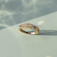 a yellow gold ring with two rows of diamonds on it's side, sitting on a white surface