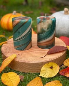 two candles sitting on top of a wooden stand surrounded by fall leaves and pumpkins