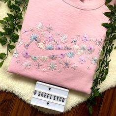 a pink shirt with flowers on it next to some green leaves and a tag that says skeelstyco