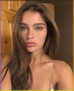 a woman with long brown hair and blue eyes is looking at the camera while wearing a necklace