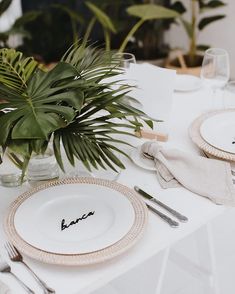 the table is set with place settings, silverware and greenery in glass vases