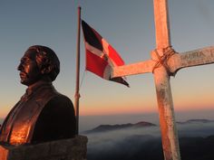 a statue with a flag on top of it next to a cross in the sky