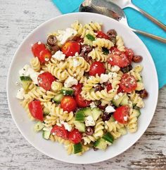 a white bowl filled with pasta salad on top of a blue napkin next to a fork