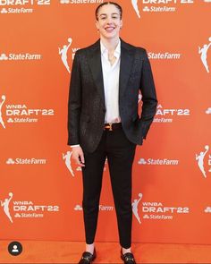 a man in a suit and tie standing on a red carpet with his hands in his pockets