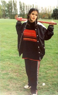 a woman holding a baseball bat on top of a green grass covered field with trees in the background