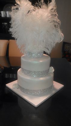 a three tiered white wedding cake with feathers on the top and side, sitting on a black table