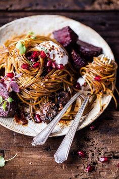 a white plate topped with spaghetti and meat covered in pomegranate next to silverware