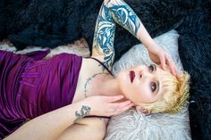 a woman in a purple dress laying on top of a white sheepskin rug with tattoos on her arms