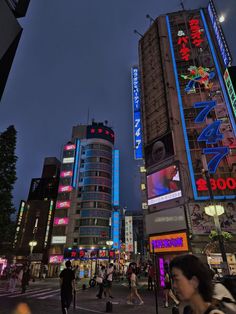 many people are walking on the street in front of tall buildings with neon signs at night