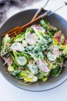 a salad with cucumbers, radishes and herbs in a gray bowl