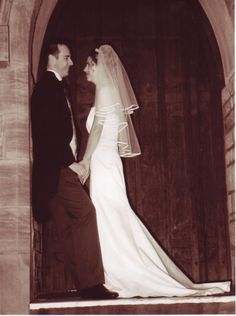 an old photo of a bride and groom standing in front of the church door, looking into each other's eyes