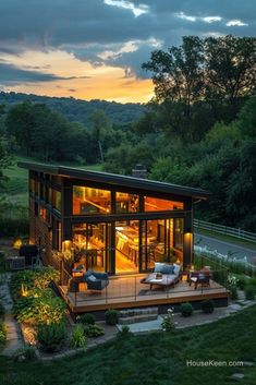 a small house in the middle of a lush green field at night with lights on