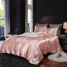 a bed with pink sheets and pillows in a room next to a lamp on a table