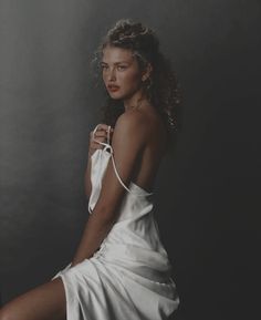 a woman in a white dress sitting on a chair with her legs crossed and one leg bent