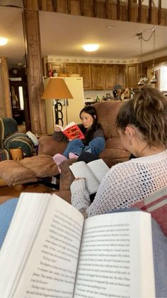 two women are sitting on the couch and reading books while another woman sits in the living room