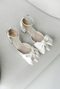 two pairs of white shoes with bows on the toes are sitting on a gray couch