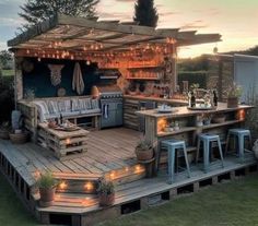 an outdoor kitchen made out of pallets with lights on the roof and stools