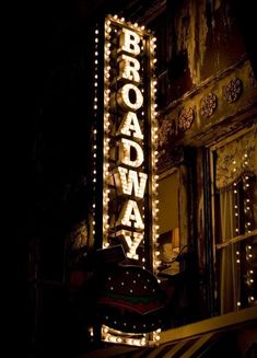 the broadway sign lit up at night in front of an old building with lights on it