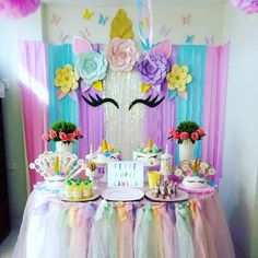 a table topped with cakes and desserts under a unicorn mask wall hanging from the ceiling