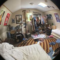 an image of a bedroom with clothes on the floor and a drum set in the corner