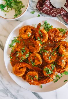 a white plate topped with shrimp covered in sauce and garnished with cilantro