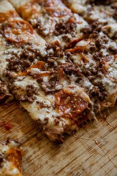 a close up of a pizza on a wooden cutting board with cheese and meat toppings