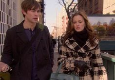 a young man and woman walking down the street in front of a building, one carrying a handbag