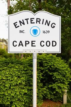 a white sign that says entering cape cod on it's side in front of some trees