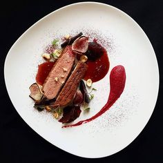 a white plate topped with meat and vegetables on top of a black table next to a red sauce