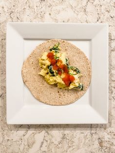 a tortilla with eggs, tomatoes and spinach on it sitting on a white plate