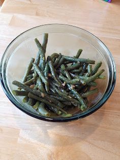 a glass bowl filled with green beans on top of a wooden table