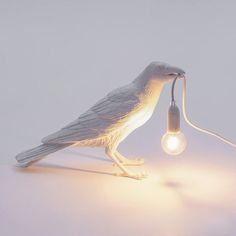 a white bird lamp sitting on top of a table next to a lightbulb