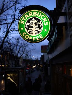 a starbucks sign hanging from the side of a building next to a sidewalk at night