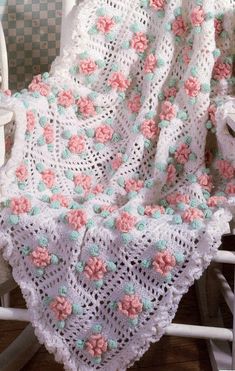 a white crocheted blanket with pink and green flowers on it sitting on a chair