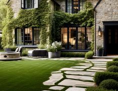 a stone house with lush green grass and plants on the front lawn, next to a fire pit