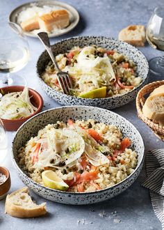 two bowls filled with rice and vegetables next to bread, wine glasses and utensils