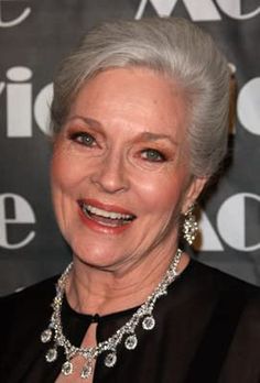 an older woman with grey hair wearing a black dress and diamond necklace smiling at the camera