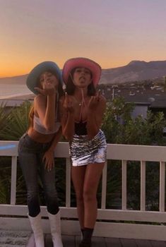 two women standing next to each other on a porch near the ocean with mountains in the background