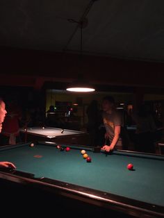 two men playing pool in a dark room with other people watching from the sidelines