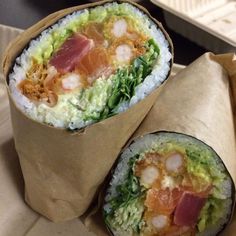 two burritos wrapped in brown paper sitting on top of a table