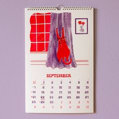 a calendar hanging on the wall with a drawing of a cat in front of a window