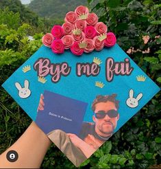 someone is holding up a blue graduation cap with flowers on it that says bye me fui