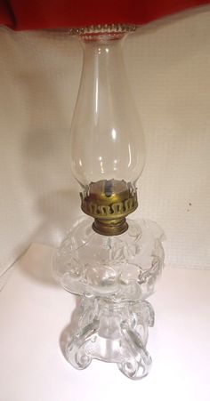 an old fashioned glass oil lamp on a white tableclothed surface with a red pillow in the background