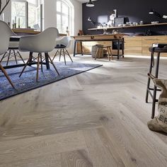 an open kitchen and dining room area with wood flooring, white chairs, and blue rug