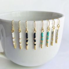 a white cup filled with lots of different colored beads and gold earwires on top of each other