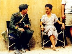 a man and woman sitting next to each other on chairs in front of a wall