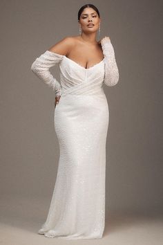 a woman in a white gown with long sleeves and an open shoulder is posing for the camera