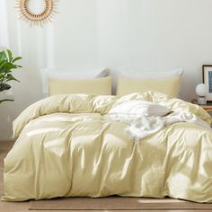 an unmade bed with yellow sheets and pillows in a white room next to a potted plant