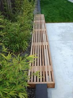 a wooden bench sitting in the middle of a garden next to some bushes and grass