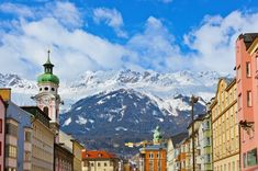 the mountains are in the distance behind some buildings and people walking down the street with snow on them